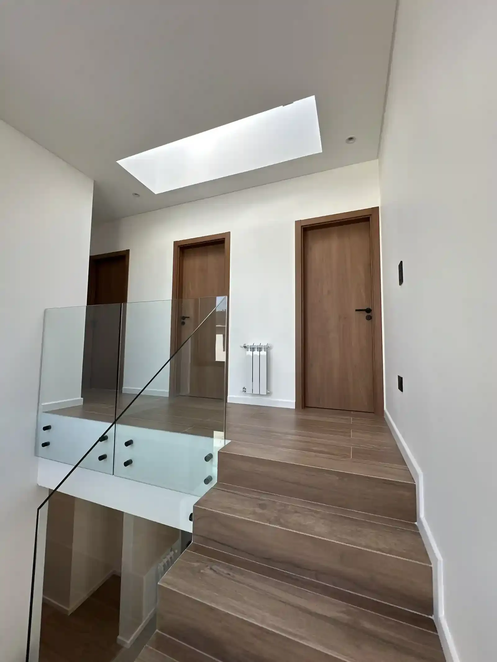 Palier de planta alta de Casa Adrogué con iluminación cenital y puertas de madera