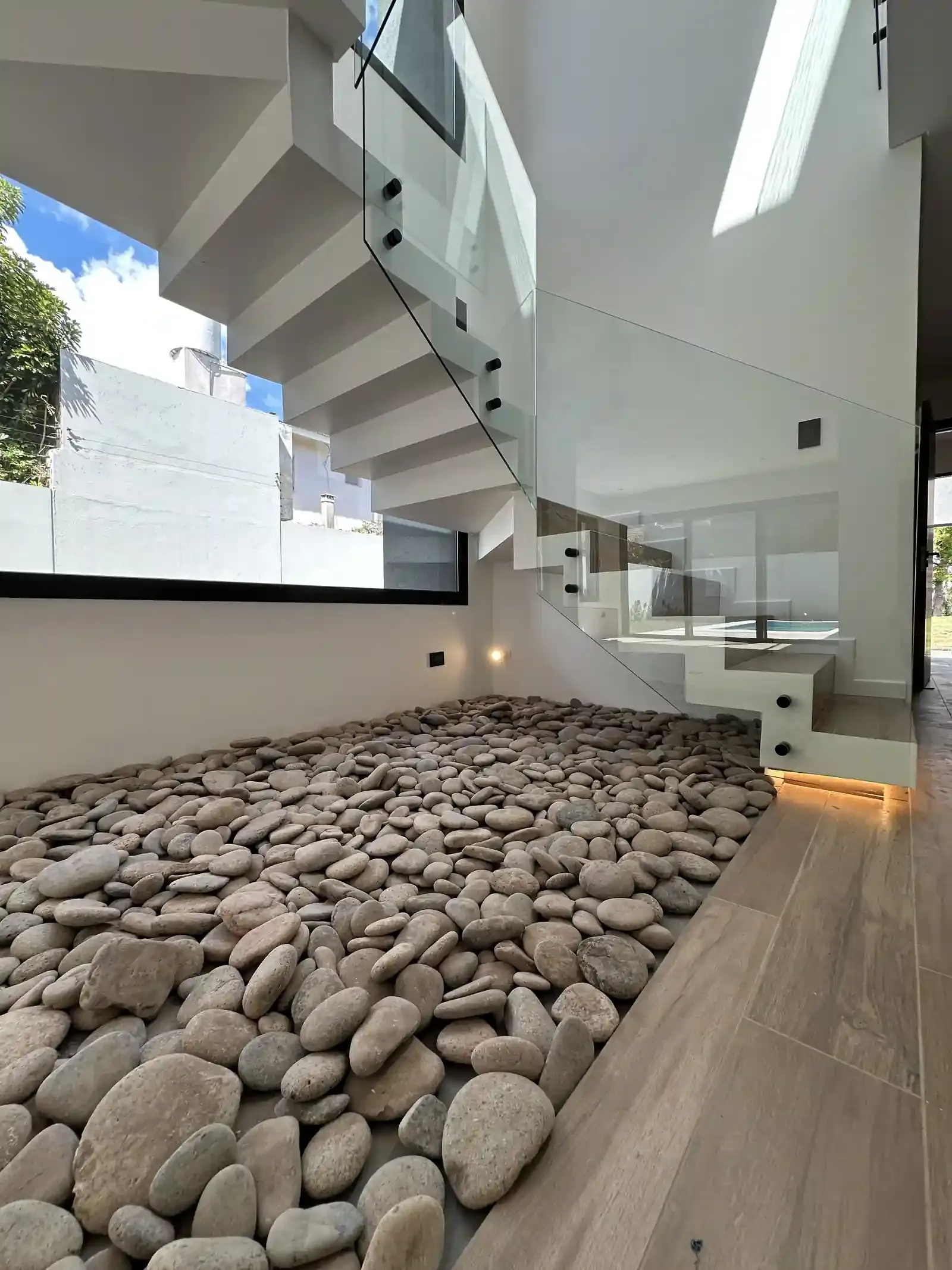 Casa Adrogué, escalera de madera y vidrio sobre cantero de canto rodado