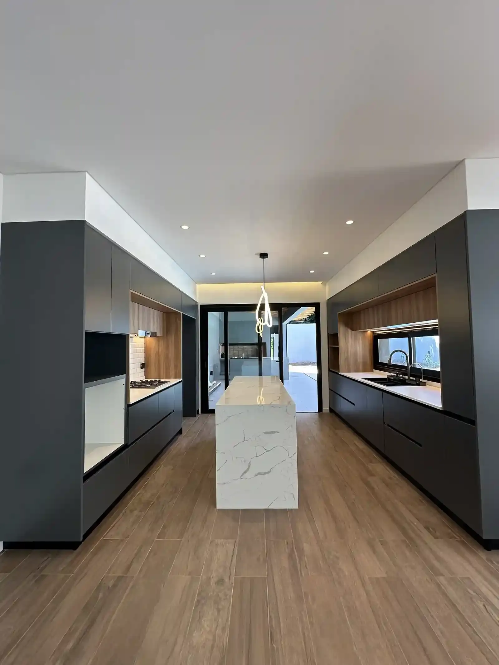 Cocina de Casa Adrogué abierta hacia el comedor, con isla de cuarzo y frentes en grafito y madera