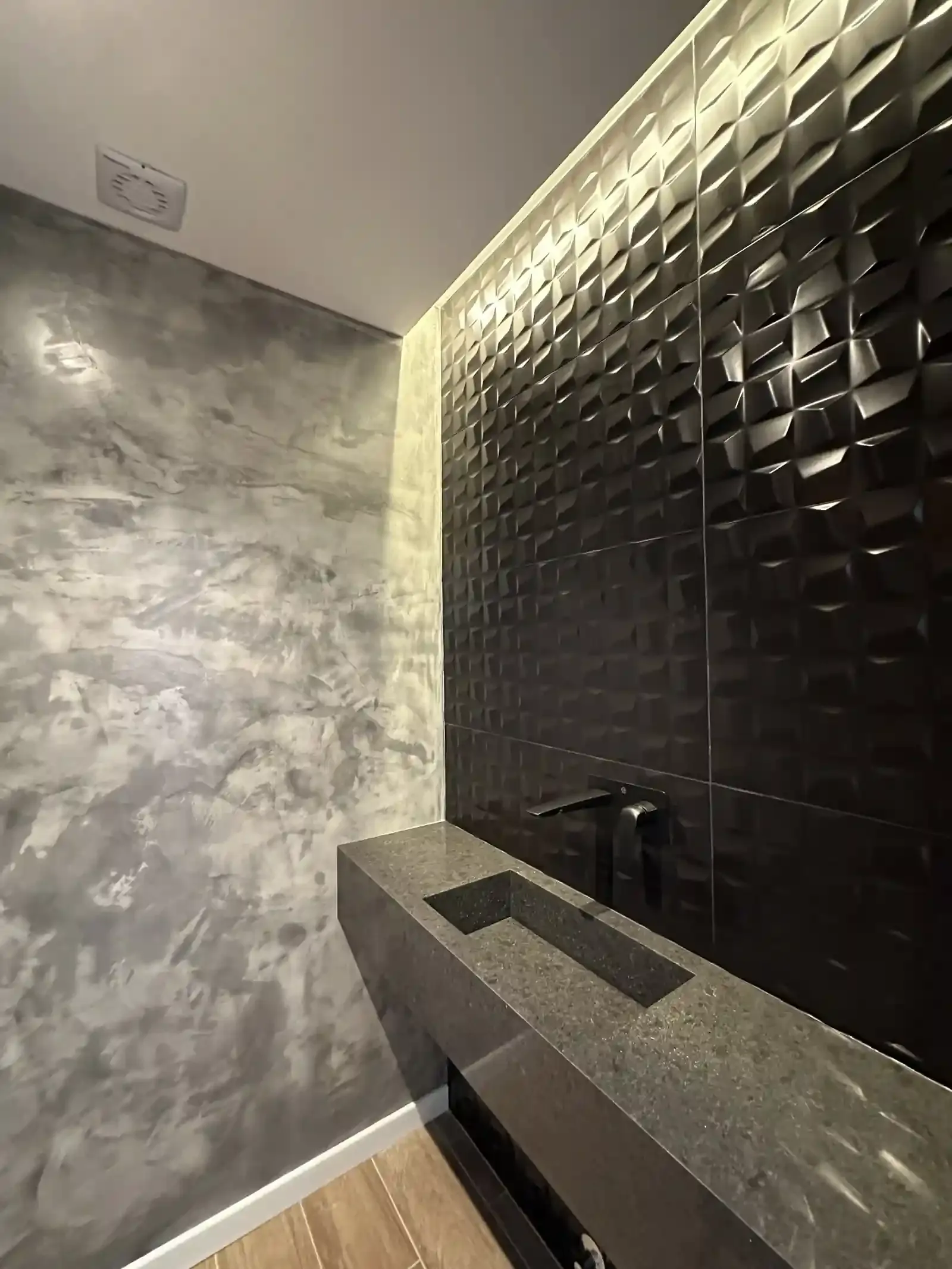 Toilette de Casa Adrogué en microcemento con bacha de piedra y cerámica negra tridimensional
