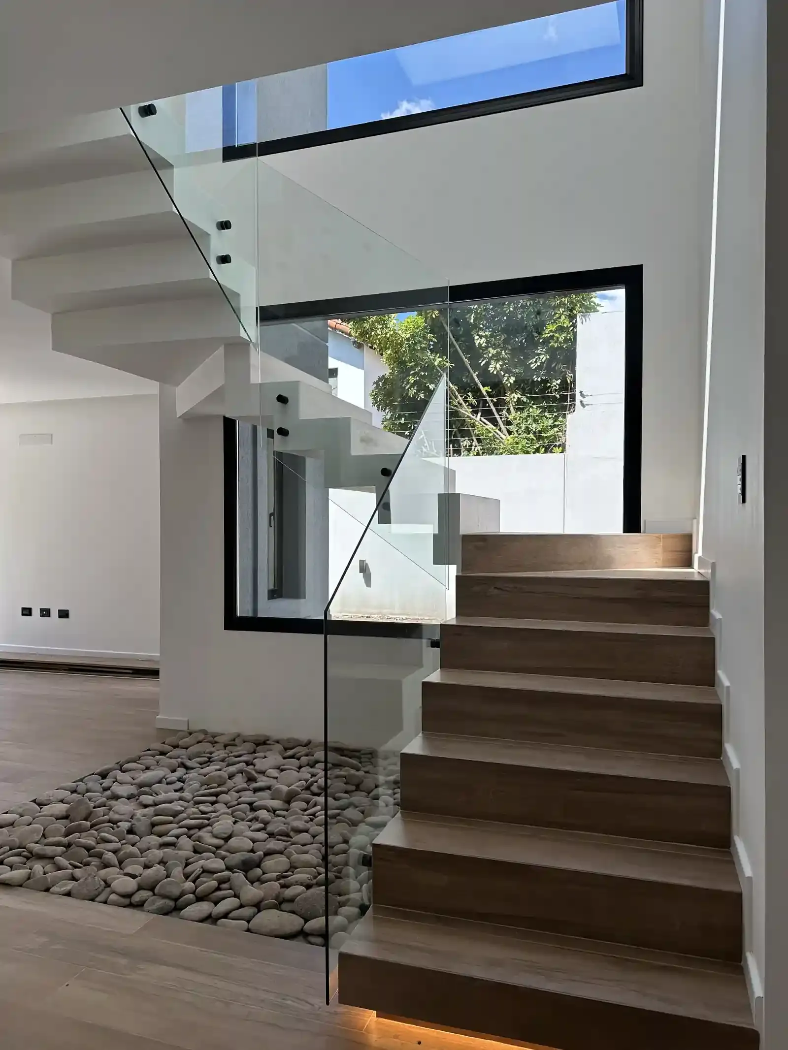 La doble altura de la escalera de Casa Adrogué con ventanal al verde