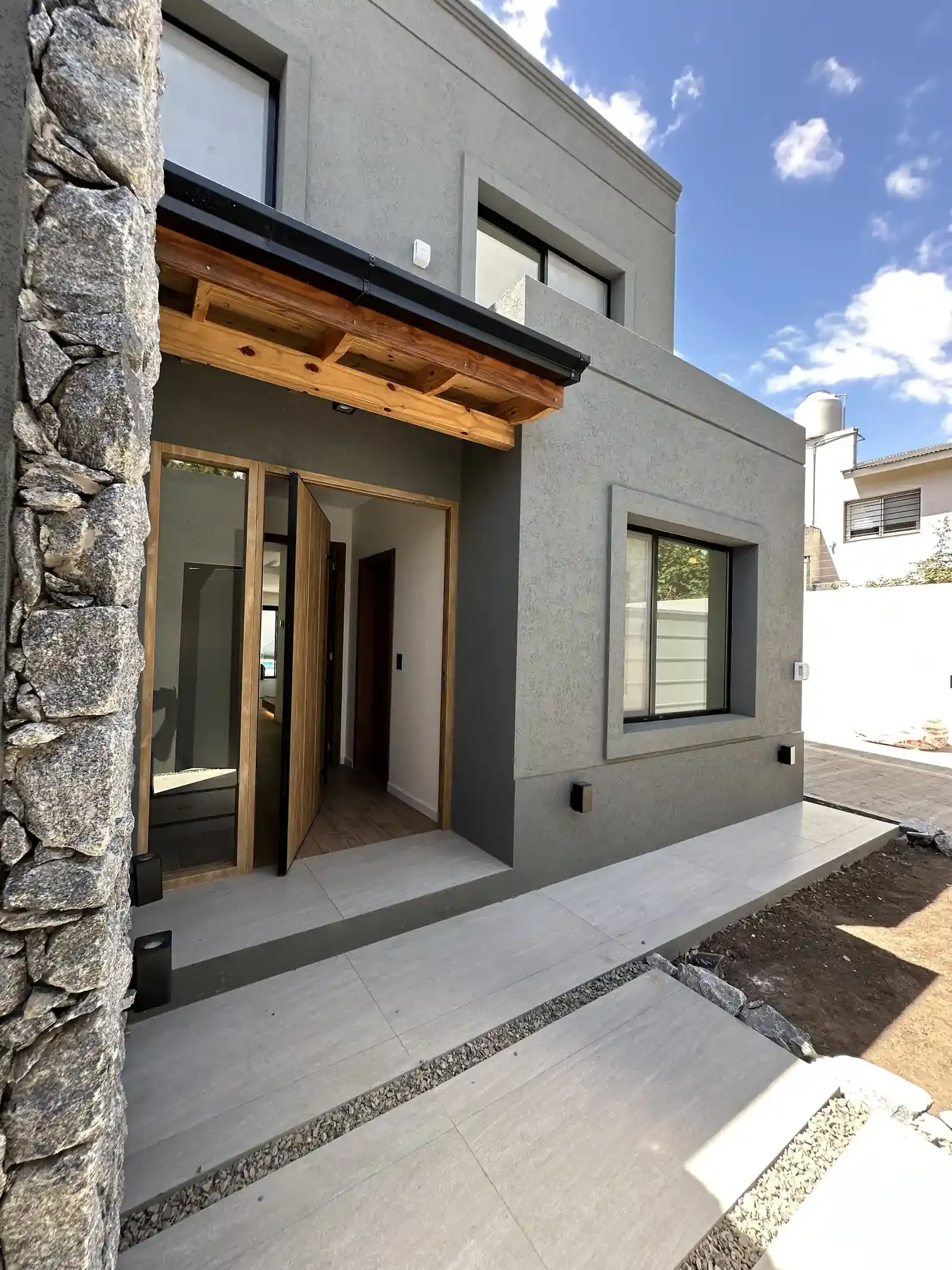 Acceso de Casa Adrogué con muro de piedra, madera y hormigón